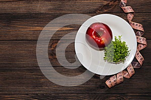 An apple with microgreen on an empty white plate with a tape measure to measure the figure. Diet and raw food concept.