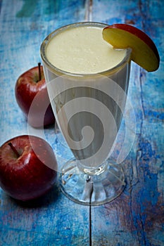 Apple milkshake in a glass and apples scattered on a wooden table.