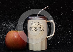 Apple with a mug on a black background. A Cup with a straw and the words Good morning on a dark background