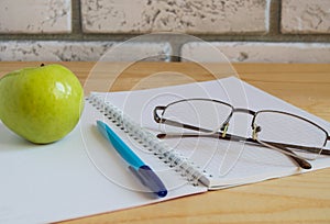 Apple, notebook, reading glasses and pen on wooden table. Back to school concept