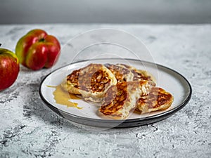 Apple pancakes and dessert fork on a light plate and red and yellow apples