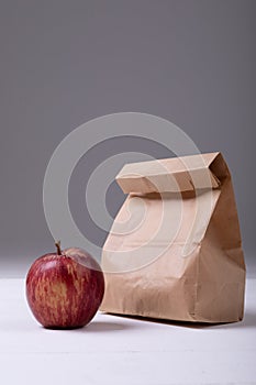 Apple and paper lunch bag on table against gray background with copy space