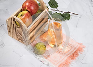 Apple and pear juice in a glass glass, apples in a wooden box on a light background.