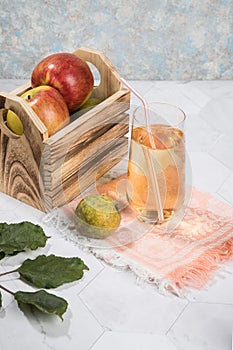 Apple and pear juice in a glass glass, apples in a wooden box on a light background.