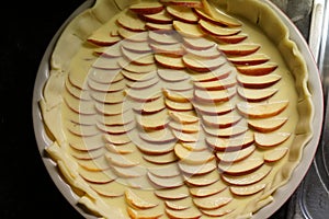 Apple pie before baking in a white ceramic baking form with neat  rows of apple slices covered by glaze