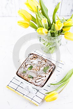 Apple pie in dishes on a white background and a bouquet of spring yellow tulips. Homemade pastries with fruit for a delicious