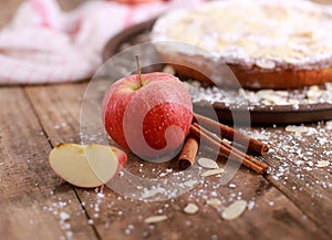 Apple pie - fresh apples and cinnamon sticks in front of a homemade apple pie on a rustic wooden table