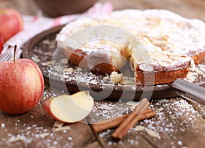 Apple pie - fresh apples and cinnamon sticks in front of a homemade apple pie on a rustic wooden table