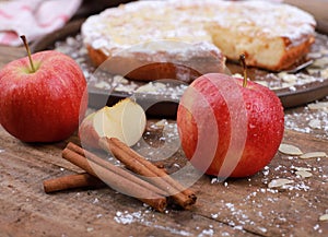 Apple pie - fresh apples and cinnamon sticks in front of a homemade apple pie on a rustic wooden table