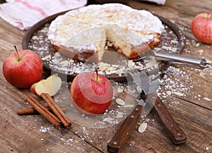 Apple pie - fresh apples and cinnamon sticks in front of a homemade apple pie on a rustic wooden table