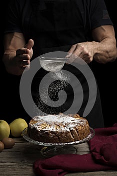 Apple pie with icing sugar on dark background and man in apron