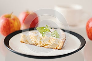 Apple pie with powdered sugar and fresh mint leaves served with whole apples and a cup of tea