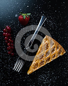 Apple pie slice on black table with currant and strawberry