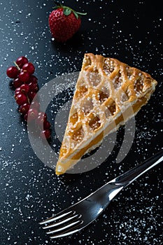 Apple pie slice on black table with currant and strawberry