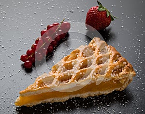 Apple pie slice on black table with currant and strawberry