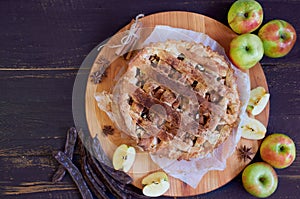 Apple pie with spices on the brown wooden board. Apple pie decorated with sliced fresh apples, carob pods and cinnamon sticks