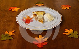 Apple pie on a white plate on a wooden table decorated with colorful autumn leaves.