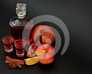 Apple pomegranate liqueur with cinnamon and anise, strong homemade alcohol in two glasses and a bottle on a black background