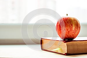 An apple on the red book near the window. Enpty space for text.