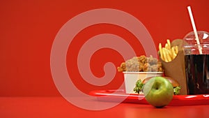 Apple rolling near fast food set, concept of choosing healthy food or unhealthy