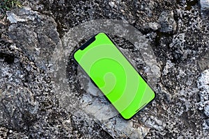 Apple's smartphone rests on a natural natural rock, with a green screen. Top view