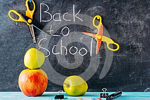 Apple, scissors and school supplies against blackboard with `back to school` on background