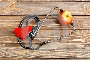 Apple, stethoscope and heart on wooden background