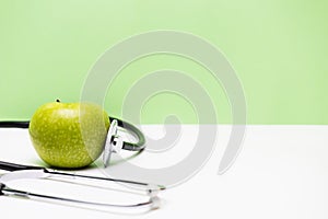 Apple and stethoscope on horizontal green and white background