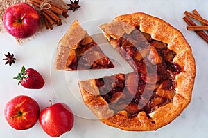 Apple strawberry autumn pie, above view table scene with cut slice over white marble