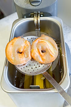 Apple turnovers on spoon above frying oil