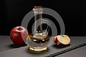 Apple vinegar in a glass bottle and fresh red apples on a stone board