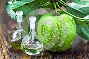 Apple vinegar in glass jar with ripe green fruit. Bottle of apple organic vinegar on wooden background. Healthy organic food.