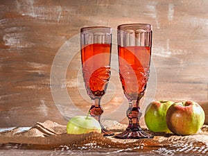 Apple wine in two pink glasses and ripe apples on craft paper