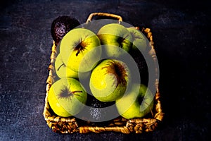 Apples and avocados in wicker platter on black surface