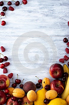 Apples, bananas, peaches, apricots, petioles, raspberries on a light gray background