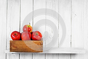 Apples in a box on wooden shelf.