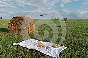 Apples, croissants, baguettes and fruits lie on a picnic tablecloth against the background of rolls of hay