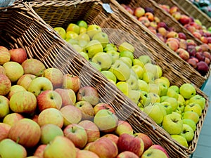 Apples of different varieties lie in a wicker box on a grocery shelf. Close-up of fruit in a supermarket. Fresh apples