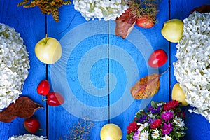 Apples, flowers, leaf litters and plums on a blue wooden table