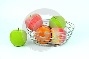 Apples and oranges in a decoratively wire basket put on isolated white background and there is an apple outside the wire basket.