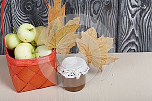 Apples in a red wicker basket. Jam in jars, apples and dried maple leaves are nearby. Fruit harvest