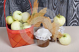 Apples in a red wicker basket. Jam in jars, apples and dried maple leaves are nearby. Fruit harvest