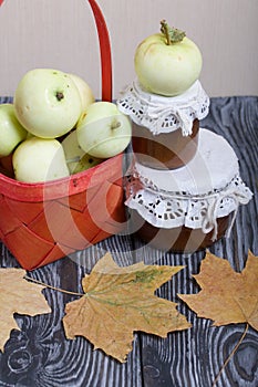 Apples in a red wicker basket. Jam in jars, apples and dried maple leaves are nearby. Fruit harvest