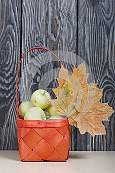 Apples in a red wicker basket. Nearby are dried maple leaves. Fruit harvest