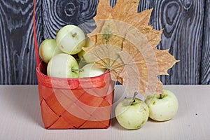 Apples in a red wicker basket. Nearby are apples and dried maple leaves. Fruit harvest