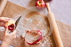 Woman`s hands peeling an apple. Baking ingredients placed on table, ready for cooking. Concept of food preparation, white table o