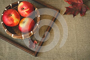 Apples in a small basket and two autumnal leaves with wooden frame. Fall background with copy space