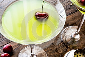 Appletini Cocktail with cherry on wooden surface.