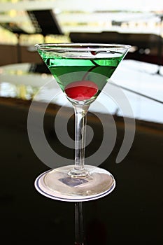 appletini cocktail with red cheries inside, vodka, pineapple juice, liqueur in classic martini cocktail glass