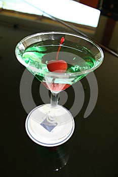 appletini cocktail with red cheries inside, vodka, pineapple juice, liqueur in classic martini cocktail glass